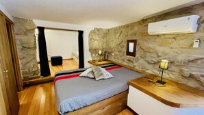 Ein Schlafzimmer mit einem Bett, Nachttischen, einer Lampe, einer Klimaanlage, einer Steinwand und einem Holzboden.