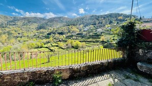 Eine Steinmauer mit einem Metallgeländer blickt auf terrassenförmig angelegte Felder und eine gebirgige Landschaft.