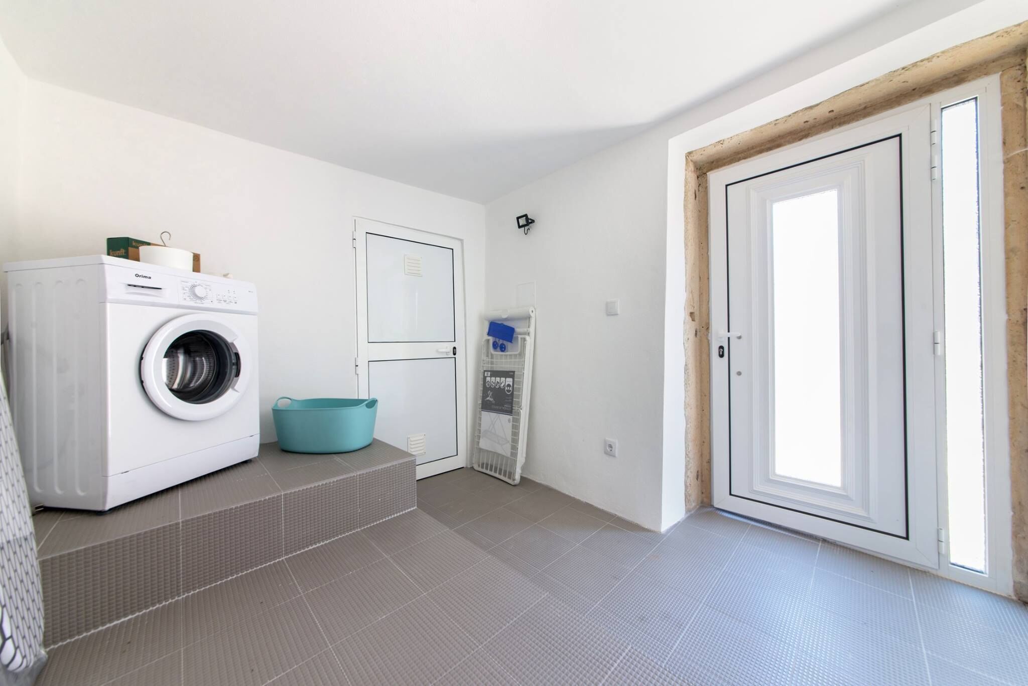A laundry room with a washing machine, a blue basin, and a drying rack.