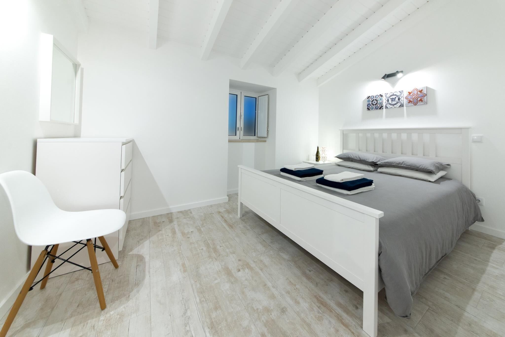 Een moderne slaapkamer met een wit bed, een nachtkastje, een stoel en een raam.