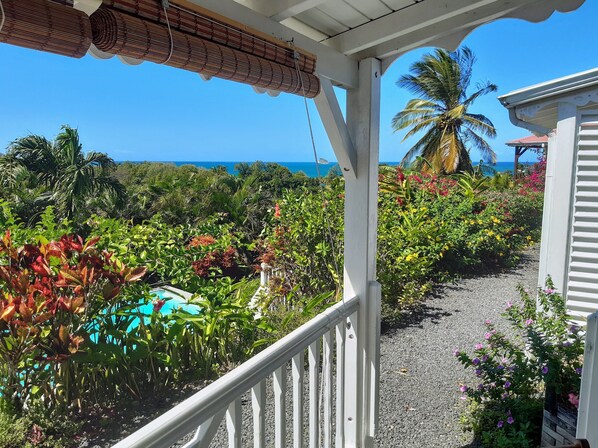 A covered outdoor area with a view of the ocean, surrounded by lush tropical vegetation and a gravel path.
