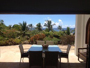 An outdoor dining area with a table and chairs, overlooking a tropical landscape with palm trees and a view of the ocean. - Beach House with private Pool and use of Tennis Court. Breathtaking Views. (Vipingo, Nr Kilifi, Vipin)