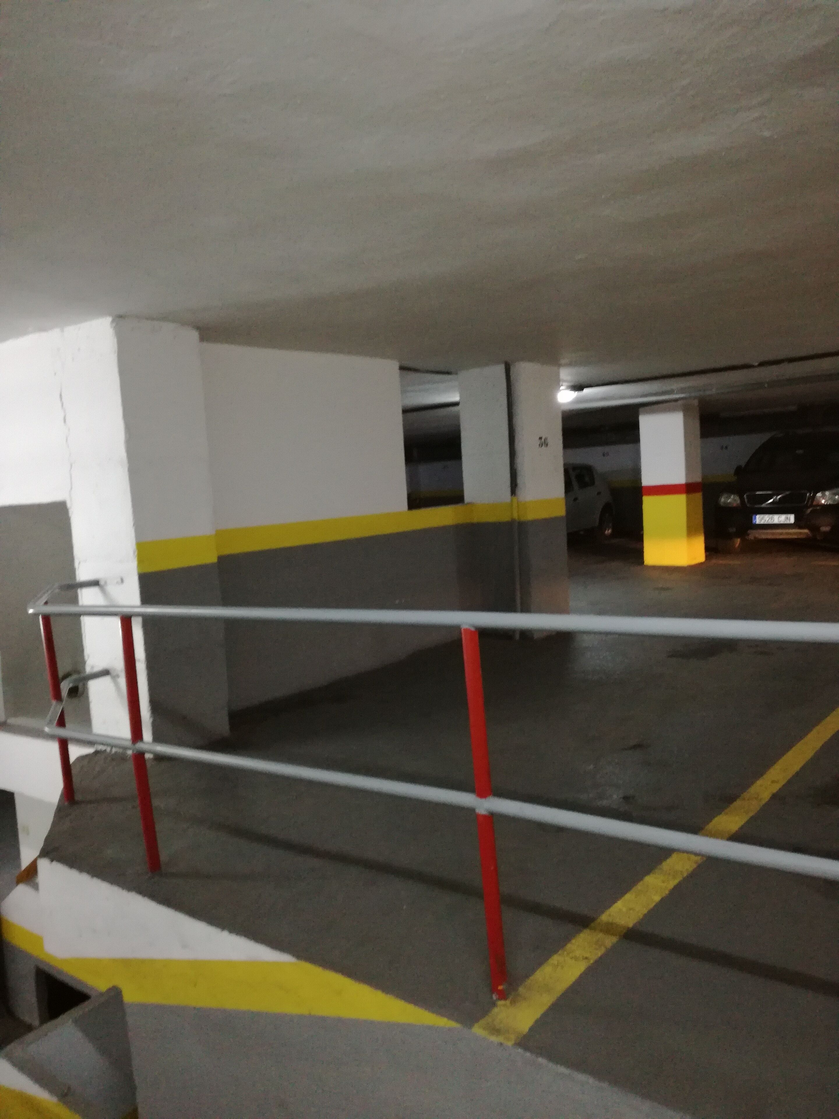 En parkeringskælder med betondæk, gule og røde sikkerhedslinjer og metalgelændere.