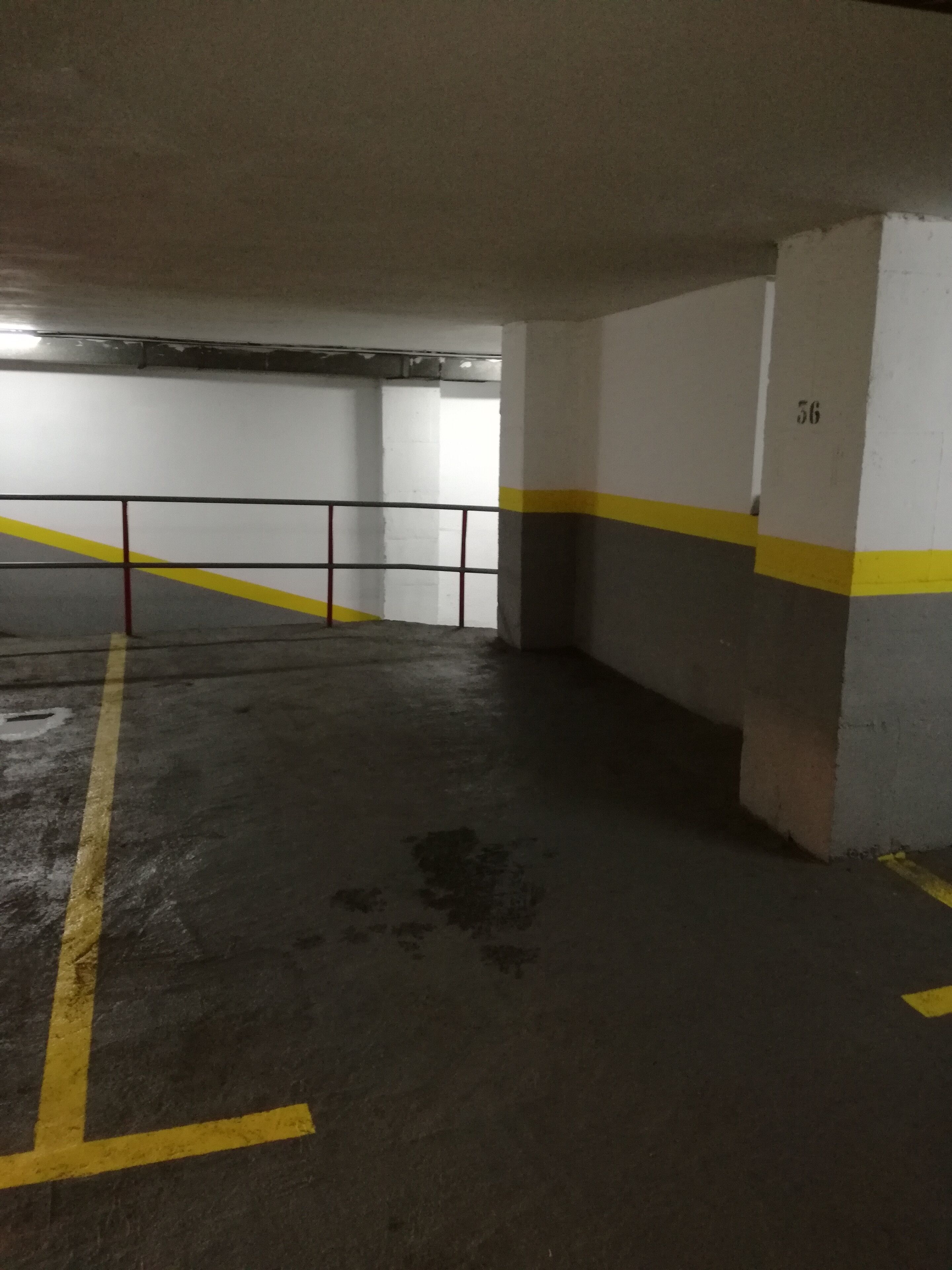 An underground parking garage with concrete walls, yellow and white painted lines, and a metal railing.