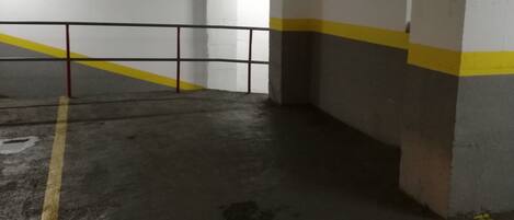 An underground parking garage with concrete walls, yellow and white painted lines, and a metal railing.