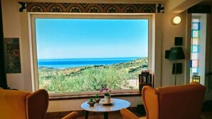 A room with two yellow armchairs facing a large window overlooking a coastal landscape. - sea view villa immersed in olive grove (sciacca)