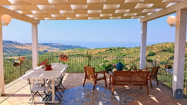 A covered outdoor seating area with a table and chairs, overlooking a scenic landscape. - sea view villa immersed in olive grove (sciacca)
