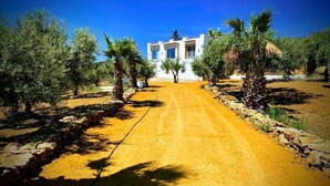 A white building with a dirt road leading to it, surrounded by trees and rocks. - sea view villa immersed in olive grove (sciacca)