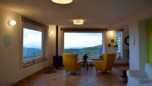 A living room with a large window, a fireplace, and yellow chairs. - sea view villa immersed in olive grove (sciacca)