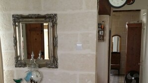 A room with a stone wall, a wooden table with a mirror, a clock, and a patterned floor. - Apartment in the heart of Vittoriosa with AC (il-Birgu)