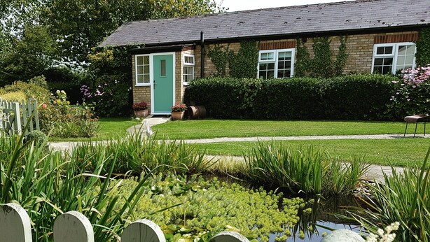 A house with a green door, a brick exterior, and a garden with a pond and flowers. - Luxury studio suite at Hawthorn Farm, kingsize bed, jacuzzi bath, private garden (Canterbury)