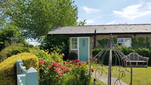 A garden with a metal trellis, a bench, and a building with a green door. - Luxury studio suite at Hawthorn Farm, kingsize bed, jacuzzi bath, private garden (Canterbury)