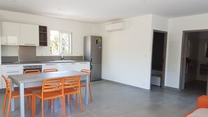 Una cocina moderna con armarios blancos, un refrigerador de acero inoxidable y una zona de comedor con una mesa gris y sillas naranjas.