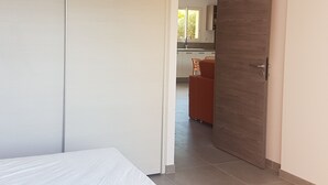 Un dormitorio con una cama, una puerta de madera y vistas a una zona de cocina con una mesa y sillas.