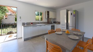 Una cocina moderna con armarios blancos, una mesa de comedor con sillas naranjas y un refrigerador.