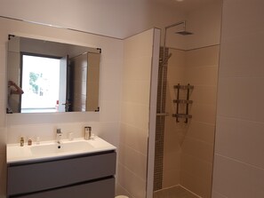 Une salle de bain avec un lavabo blanc, un miroir et une douche.