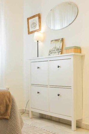A white dresser with drawers, a round mirror, a framed picture, and a floor lamp.