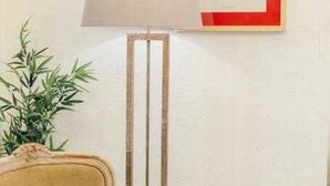 Ein Zimmer mit einem beigefarbenen Sessel, einer Stehlampe und einem gerahmten Pflanzenprint an der Wand.