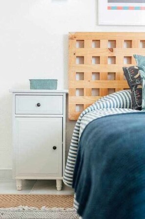 A bedroom with a bed, a nightstand, a wooden headboard, and a wall-mounted shelf.