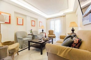 A well-lit living room with a sofa, armchairs, a coffee table, and framed artwork on the walls.