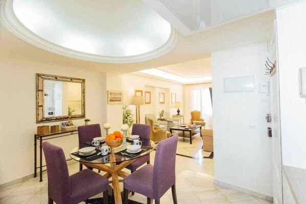 A dining area with a round table, purple chairs, and a bowl of fruit.