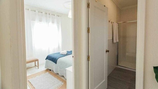 Ein Zimmer mit einem Bett, einer Duschkabine und einer Tür zu einem weiteren Raum.