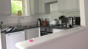 A compact kitchen with white cabinets, a window with a view of greenery, a kettle, a toaster, and a sink. - Rural Retreat in deepest Sussex (Lewes)