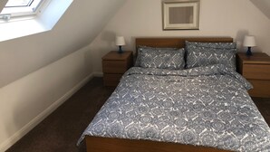 A bedroom with a sloped ceiling, a bed with patterned bedding, two bedside tables with lamps, and a framed picture on the wall. - Rural Retreat in deepest Sussex (Lewes)