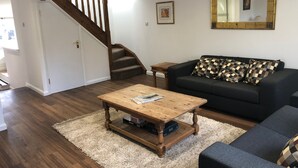 A living room with a wooden coffee table, a black sofa with patterned cushions, a staircase, and a large mirror on the wall. - Rural Retreat in deepest Sussex (Lewes)