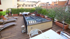 En tagterrasse med swimmingpool, liggestole og plantekasser.