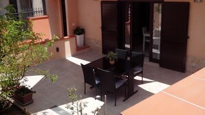 Un espace patio extérieur avec une table et des chaises, entouré de plantes en pot et agrémenté d’un parasol blanc.