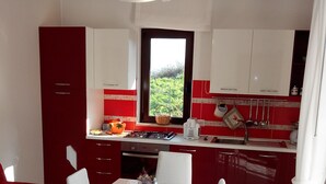 Une cuisine moderne avec des meubles blancs et rouges, une table à manger avec des chaises blanches et une fenêtre donnant sur un espace verdoyant.