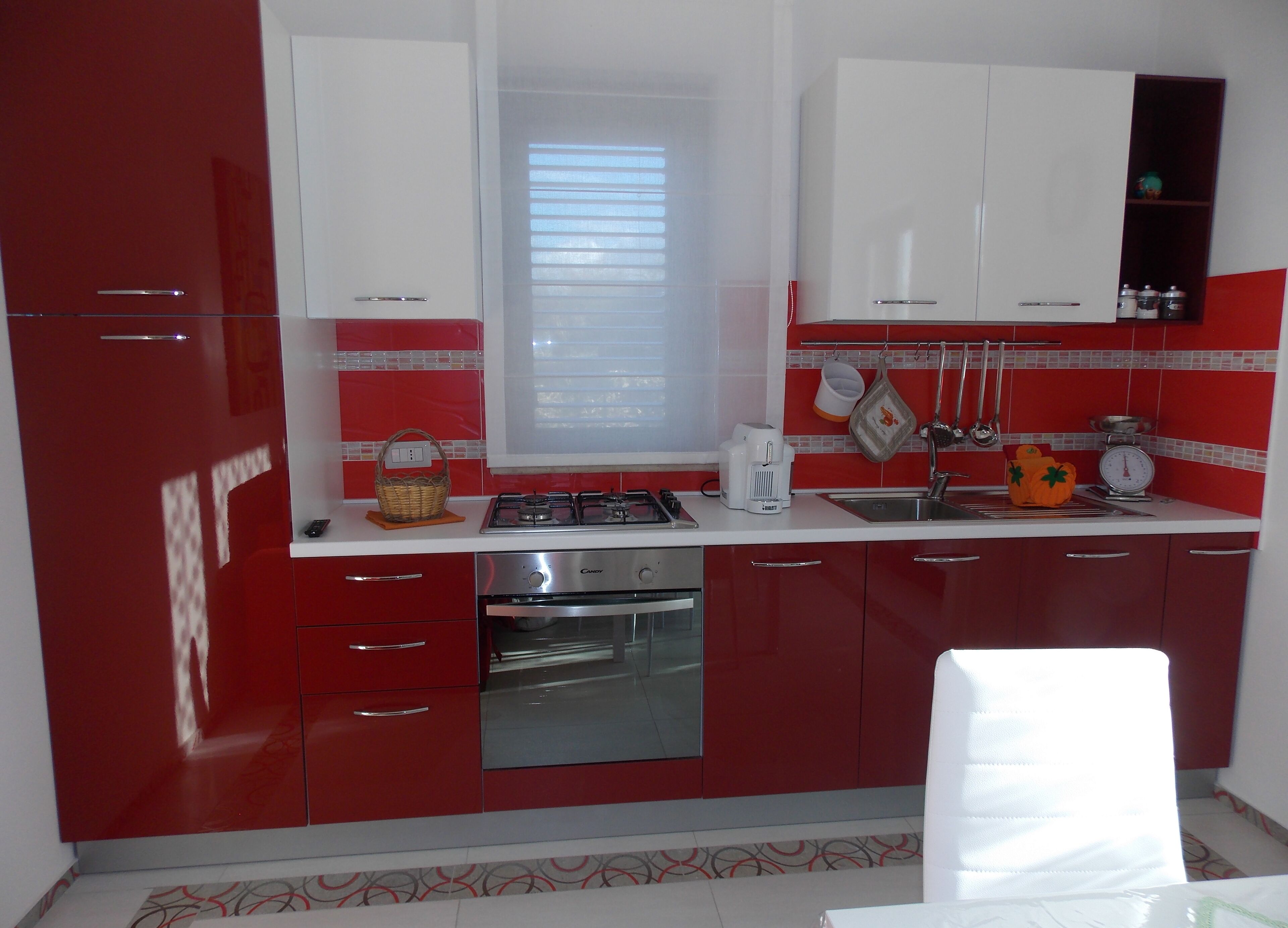 Una cocina con armarios rojo y blanco, estufa a gas, un lavabo y una ventana con persianas.