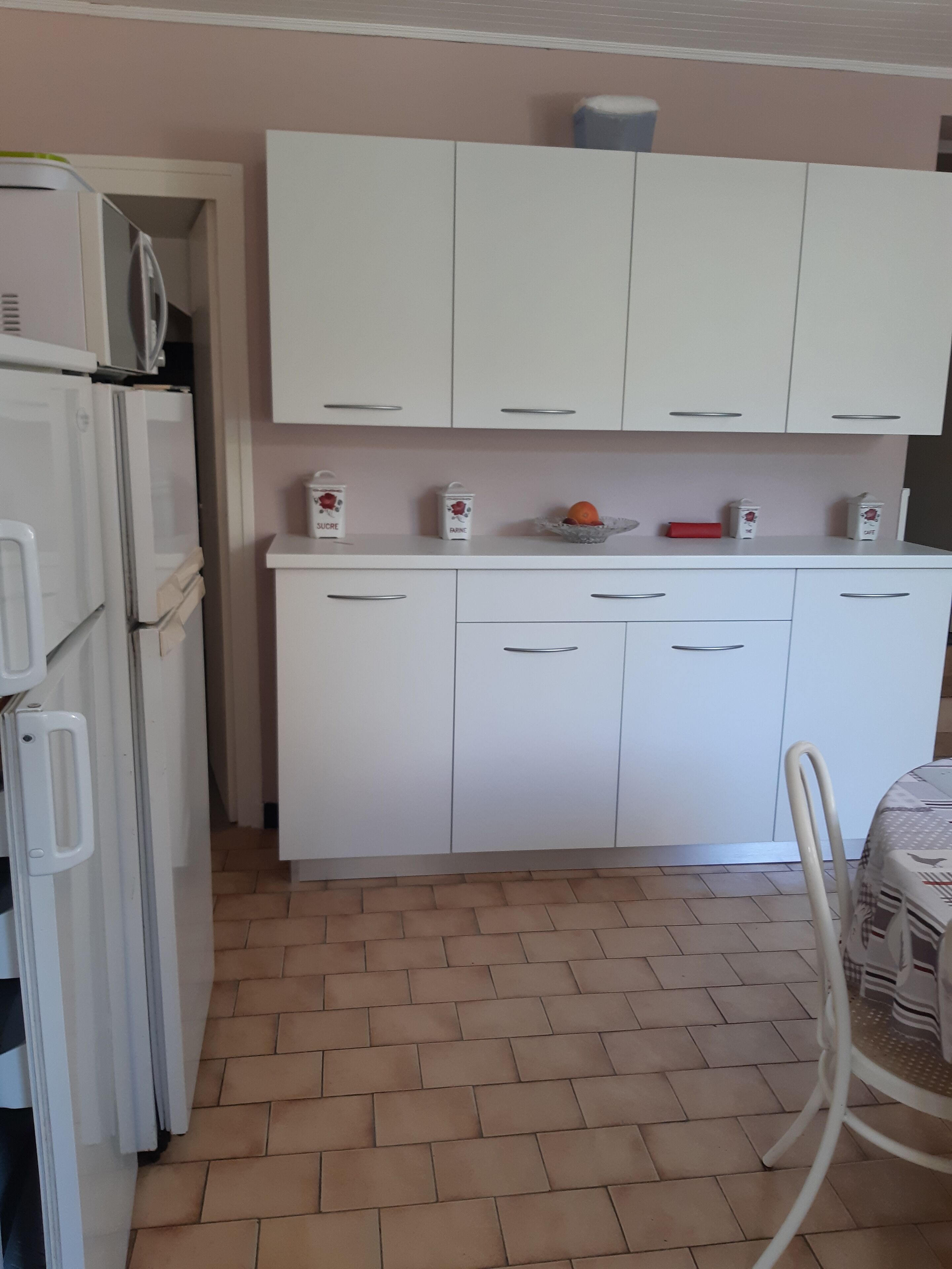 A kitchen with white cabinets, a white refrigerator, and a tiled floor.