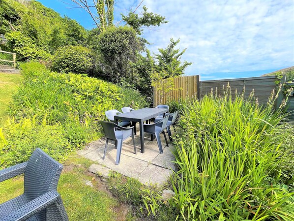 A patio with a table and chairs, surrounded by lush greenery and a wooden fence.