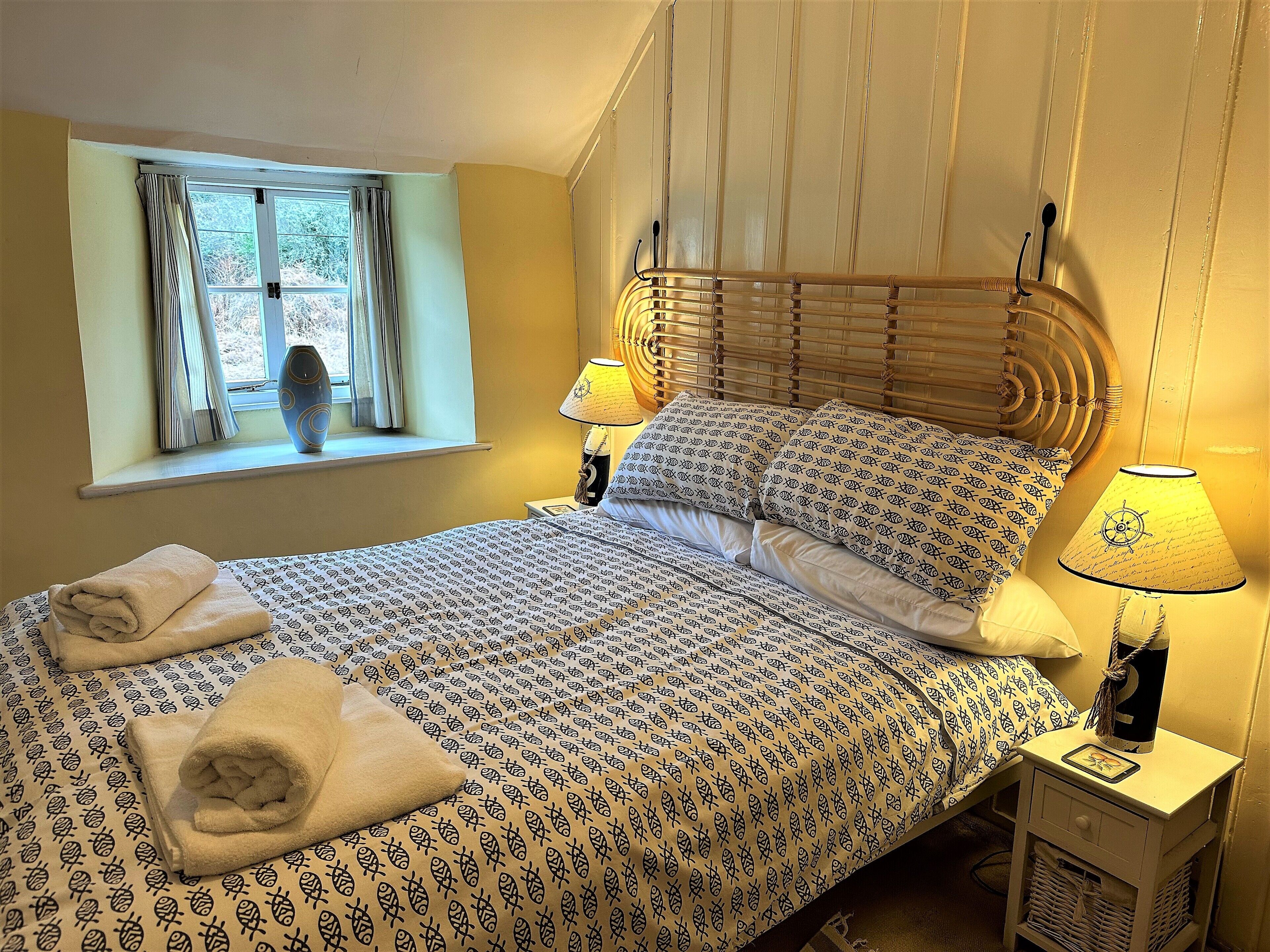 A neatly made bed with patterned bedding, two bedside lamps, a window with curtains, and a bedside table with a lamp.