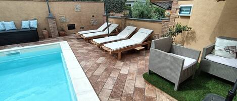 Un área de piscina con sillas de descanso y un espacio de estar techado.