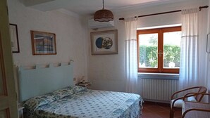 Een slaapkamer met een bed, een raam met gordijnen, een radiator en een rieten stoel.