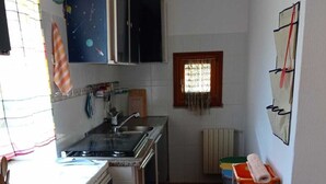 Een compacte keuken met een granieten aanrecht, een fornuis en een spoelbak. Er is een raam met gordijn, een radiator en een klein plankje met een opgerolde handdoek.