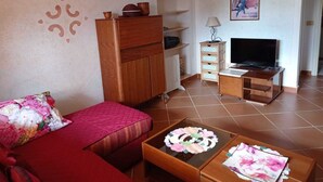 Een woonkamer met een rode bank, een houten kast, een tv op een standaard en een salontafel met bloemdecoraties.