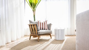 Un salon avec un fauteuil en bois, une petite table d’appoint blanche et une grande plante.
