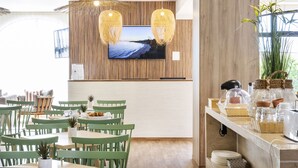 Un espace repas moderne avec des chaises vertes, un mur en bois orné d’un téléviseur et un buffet proposant divers plats.