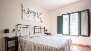 A bedroom with a bed, two bedside tables, a wall-mounted lamp, a window with curtains, and a painting on the wall. - Self catering Puerta del Agua for 6 people (Uclés)