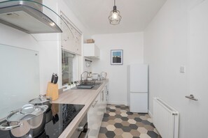 Eine moderne Küche mit einer schwarzen Induktionskochplatte, weißen Schränken, einer Holz Arbeitsplatte und einem Boden mit sechseckigem Muster.
