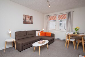 Ein modernes Wohnzimmer mit einer braunen Couch, einem kleinen weißen Tisch und einem Esstisch mit Stühlen.