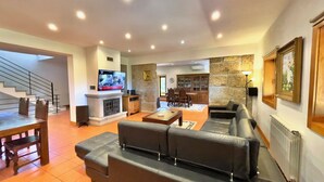 A spacious living room with a fireplace, a television, a stone accent wall, and a dining area with wooden furniture.