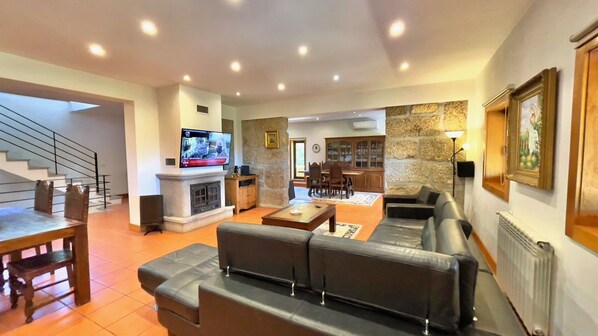 A spacious living room with a fireplace, a television, a stone accent wall, and a dining area with wooden furniture.