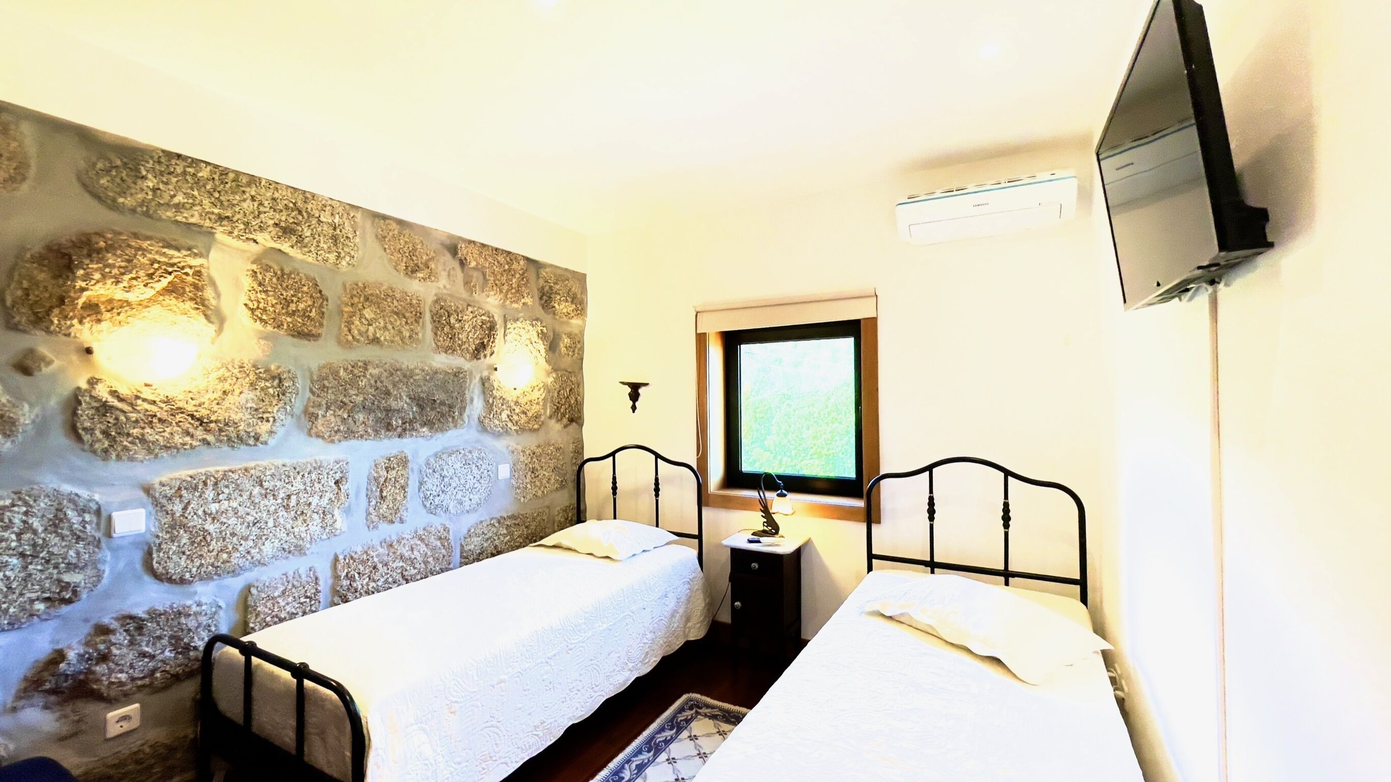 A room with two single beds, a stone wall, a television, and a window.