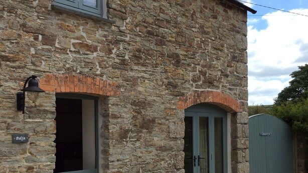 A stone building with a door and windows, a small outdoor seating area with chairs and a table, and a gate in the background. - Romantic Rural Retreat, Ideal Base to Explore Cornwall (Wadebridge)