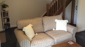 A striped sofa with pillows, a wooden staircase, a clock on the wall, and a bookshelf with books. - Romantic Rural Retreat, Ideal Base to Explore Cornwall (Wadebridge)